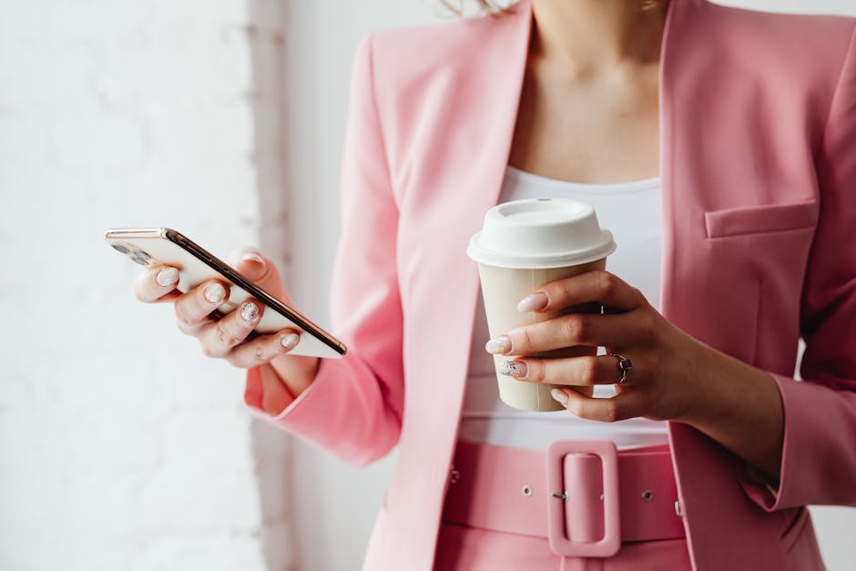 Fashionable woman with coffee cup and phone in a pink suit indoors.