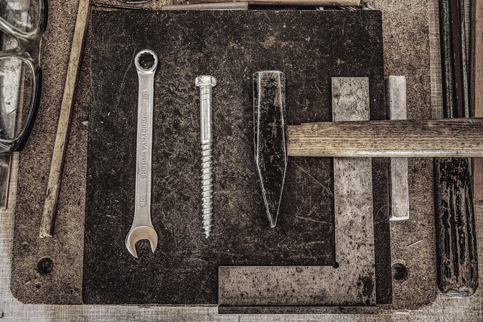 A collection of vintage workshop tools including a wrench, nail, and hammer displayed on a wooden table.