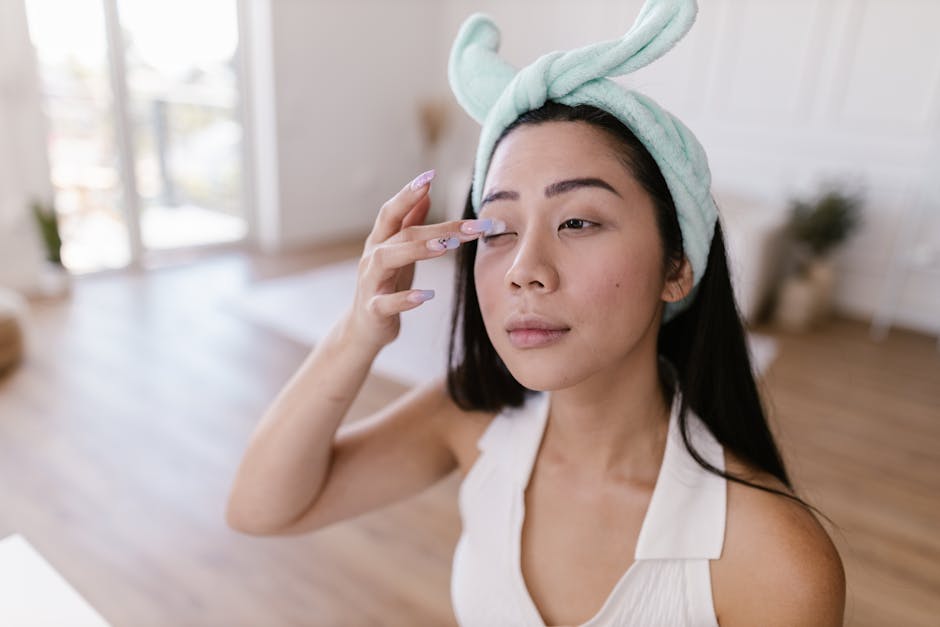Asian woman with a hairband applying makeup indoors, showcasing beauty routine.