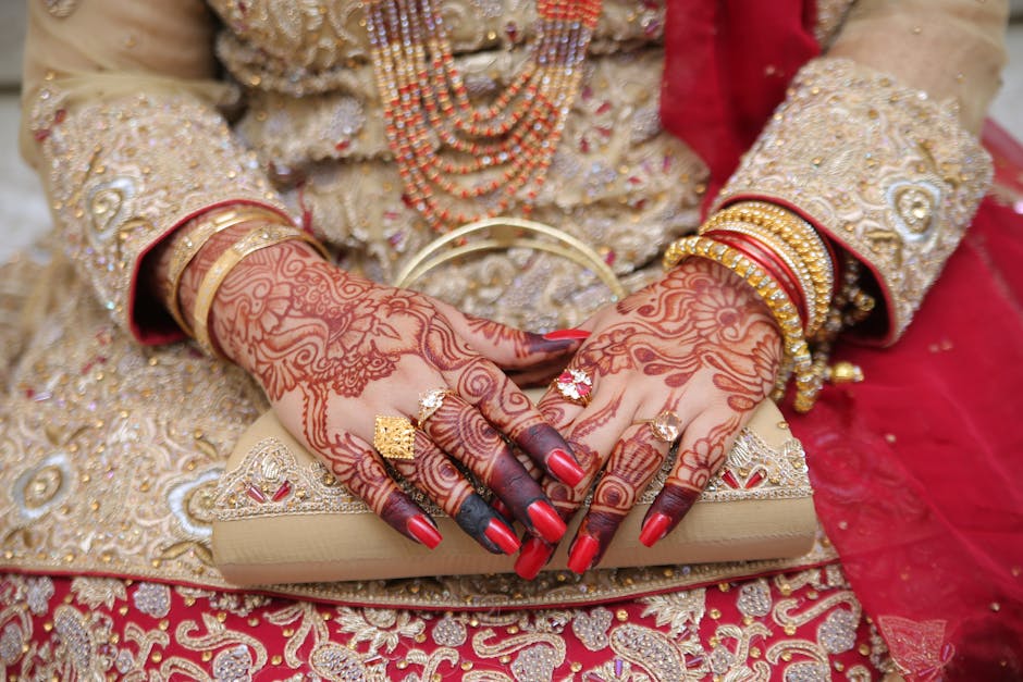 Close-up of an Indian bride's hands adorned with mehndi, jewelry, and traditional attire.