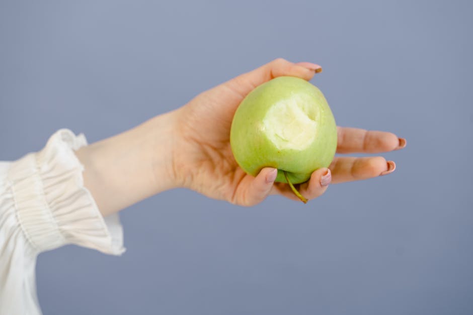 A woman holds a green apple with a bite taken out against a blue background.