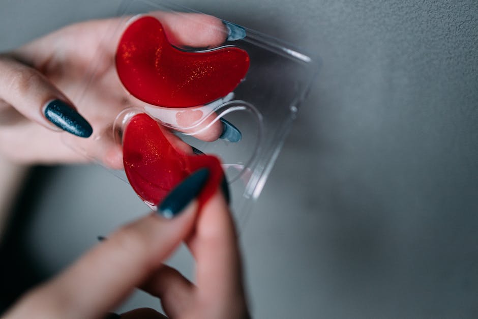 Close-up shot of red under-eye patches held by manicured hands, perfect for skincare visuals.